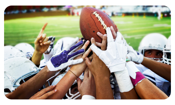 Hands of lots of players all reaching toward a football