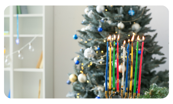 Fully lit menorah sits in front of a Christmas tree with blue and white ornaments