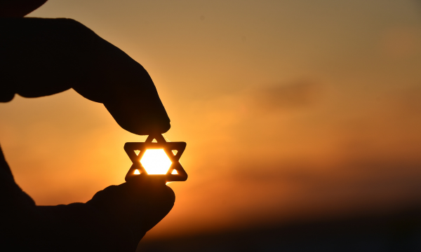 Fingers holding a star of David up to the sunset