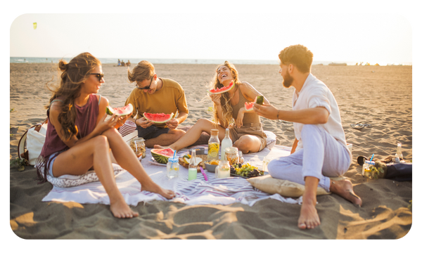 Group of friends eat watermelon on the beach during a picnic