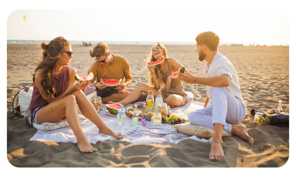 Group of friends eat watermelon on the beach during a picnic