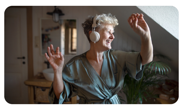 Older woman in a bathrobe and headphones dances in her room